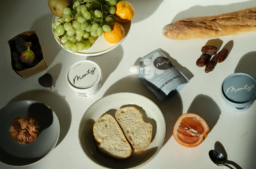 A sunlit table with Monty's butter and cream cheese, bread, and fruit
