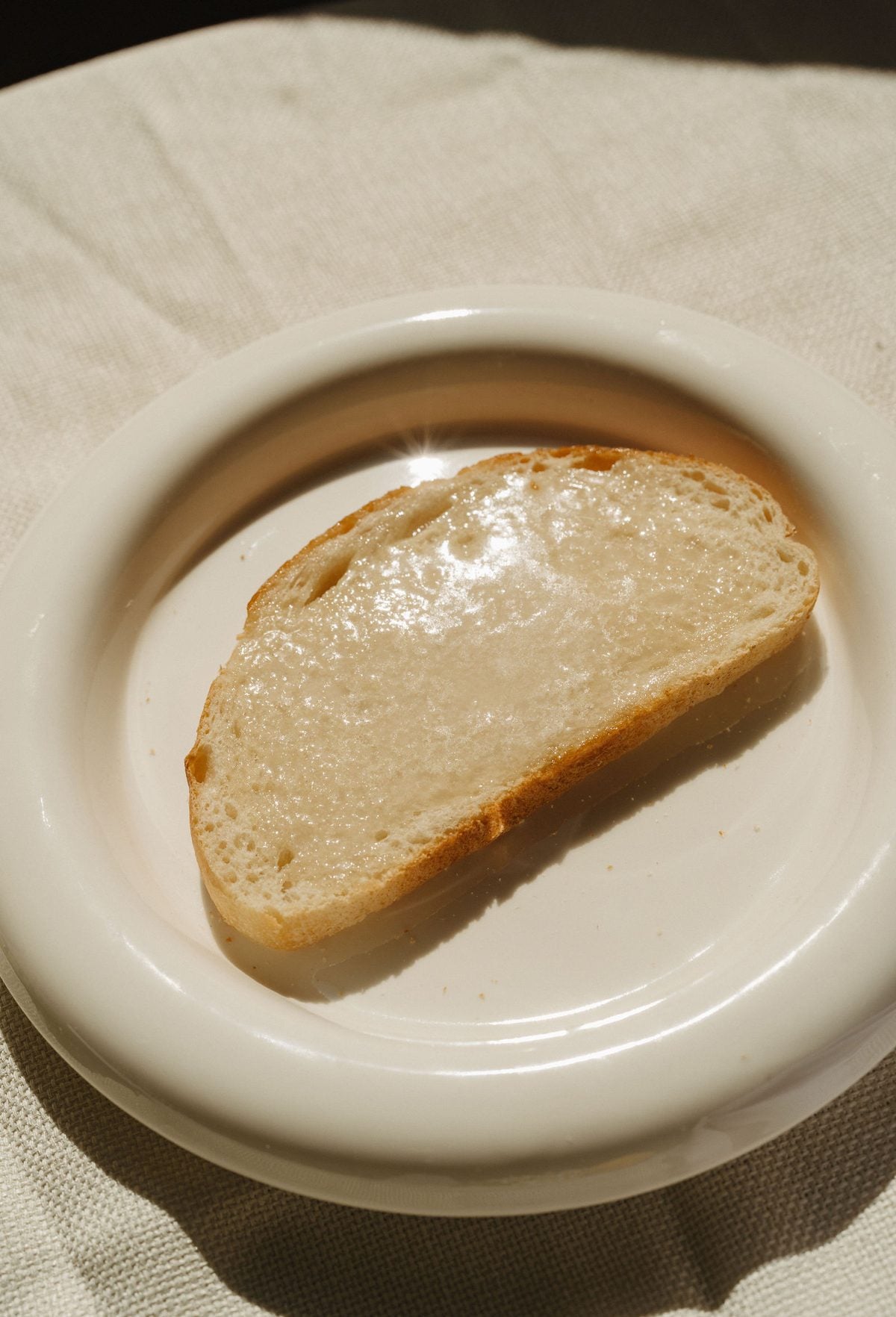 A slice of bread with melting Monty's Oat Butter on a white plate