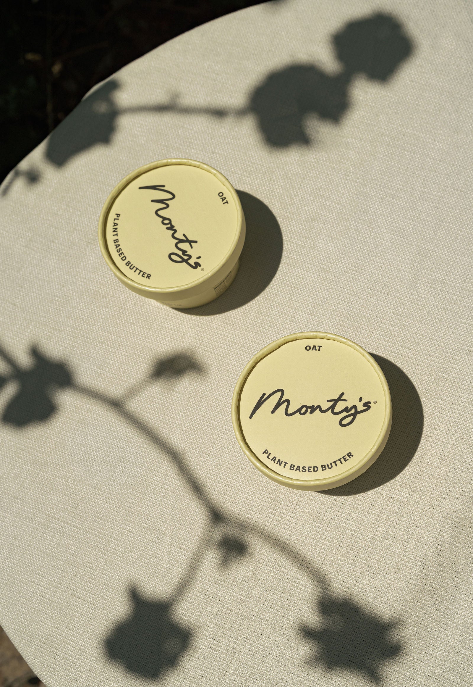 Two Monty's Oat Butter cups on a sunlit linen table with flower shadows